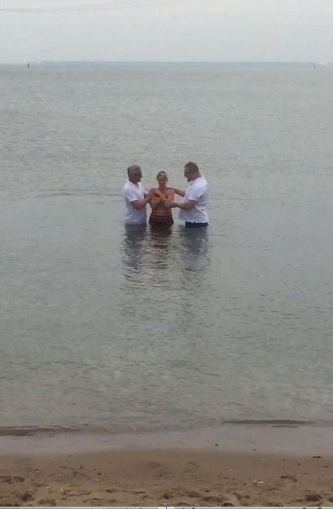 Dopeling en begeleiders in gebed, midden in het water